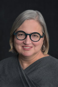 A white woman with green glasses and gray hair